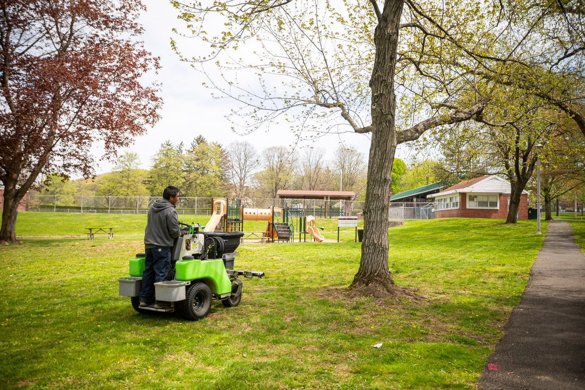 lawn care technician applies fertilizer using ride on machine
