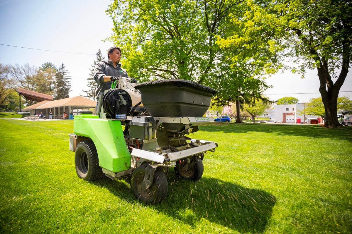 lawn care technician spreading granular lime on a lawn