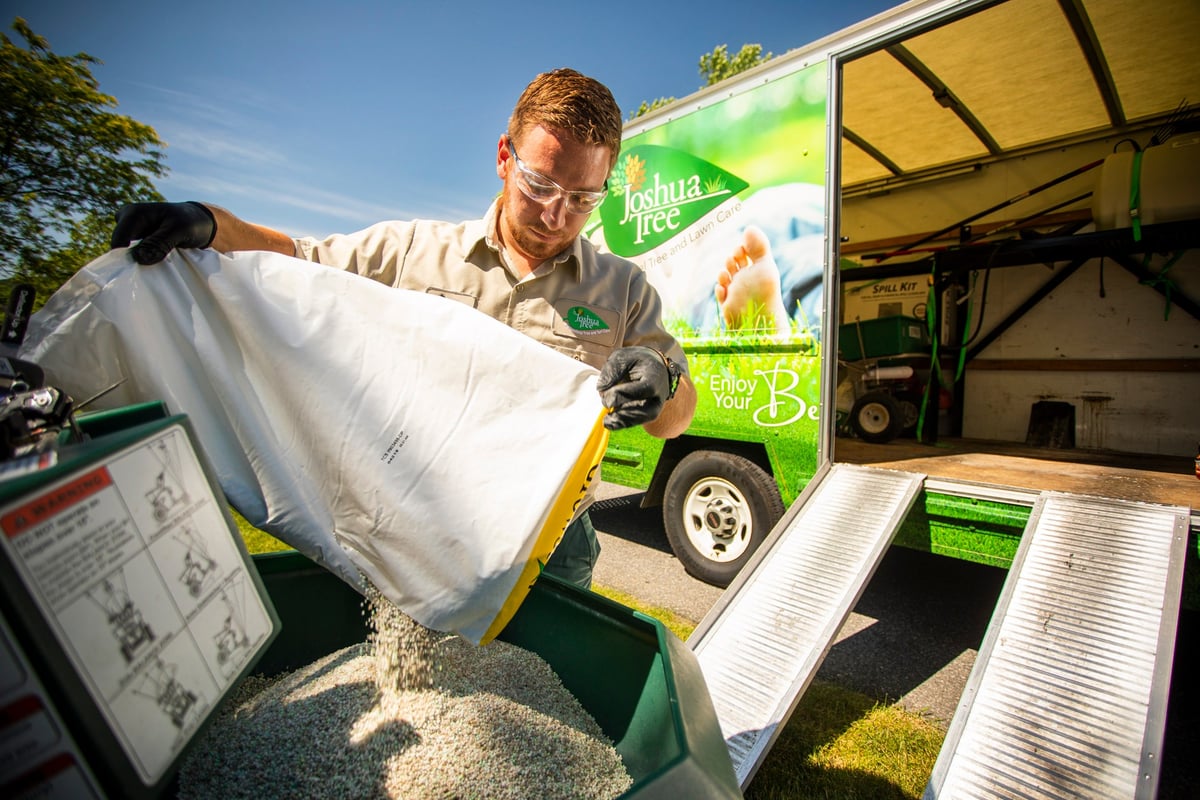 Lawn care technician pours fertilizer in spreader