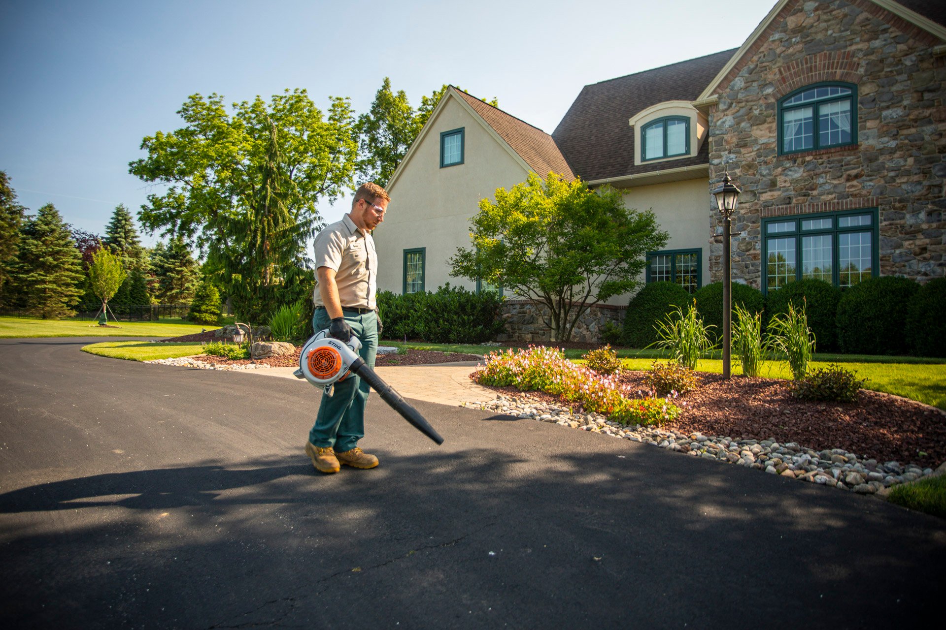 residential landscape technician blowing a driveway for spring cleanup