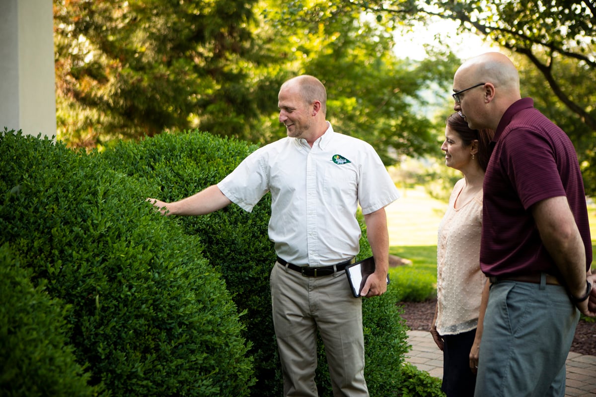 pest control technician inspects landscape with homeowners