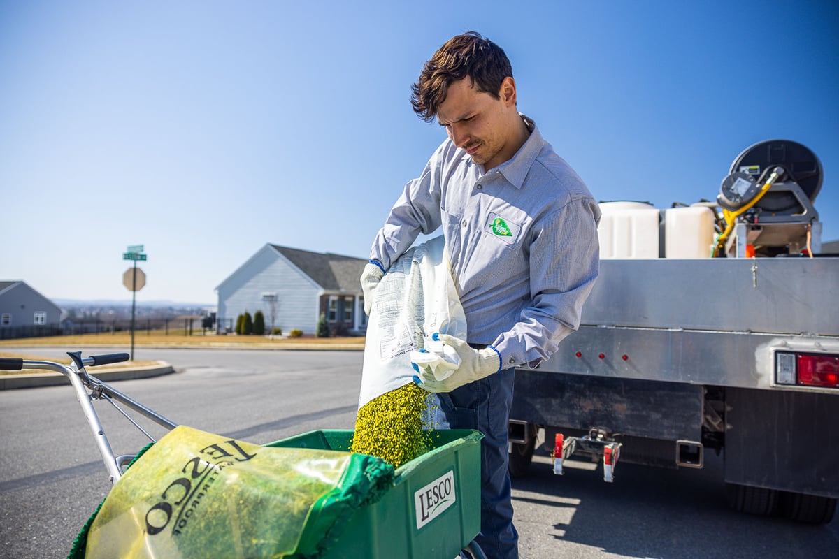 lawn care technician pours fertilizer into spreader