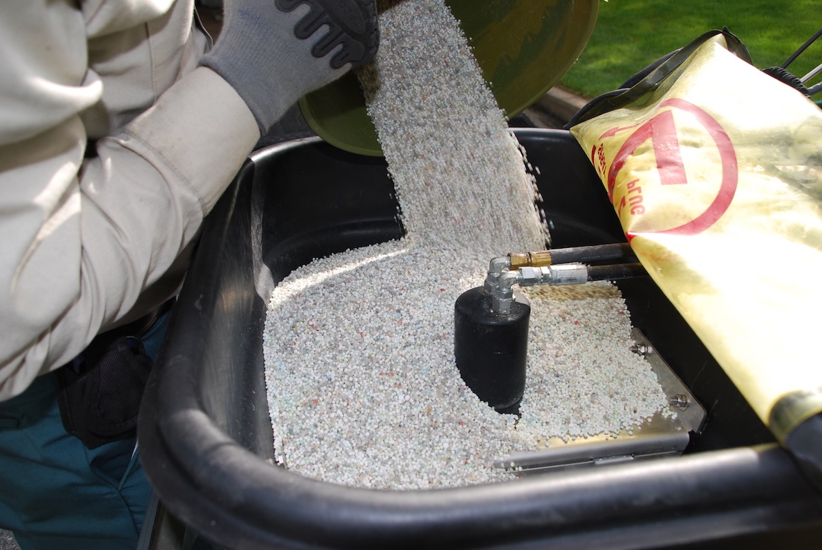 lawn care expert pours fertilizer into spreader