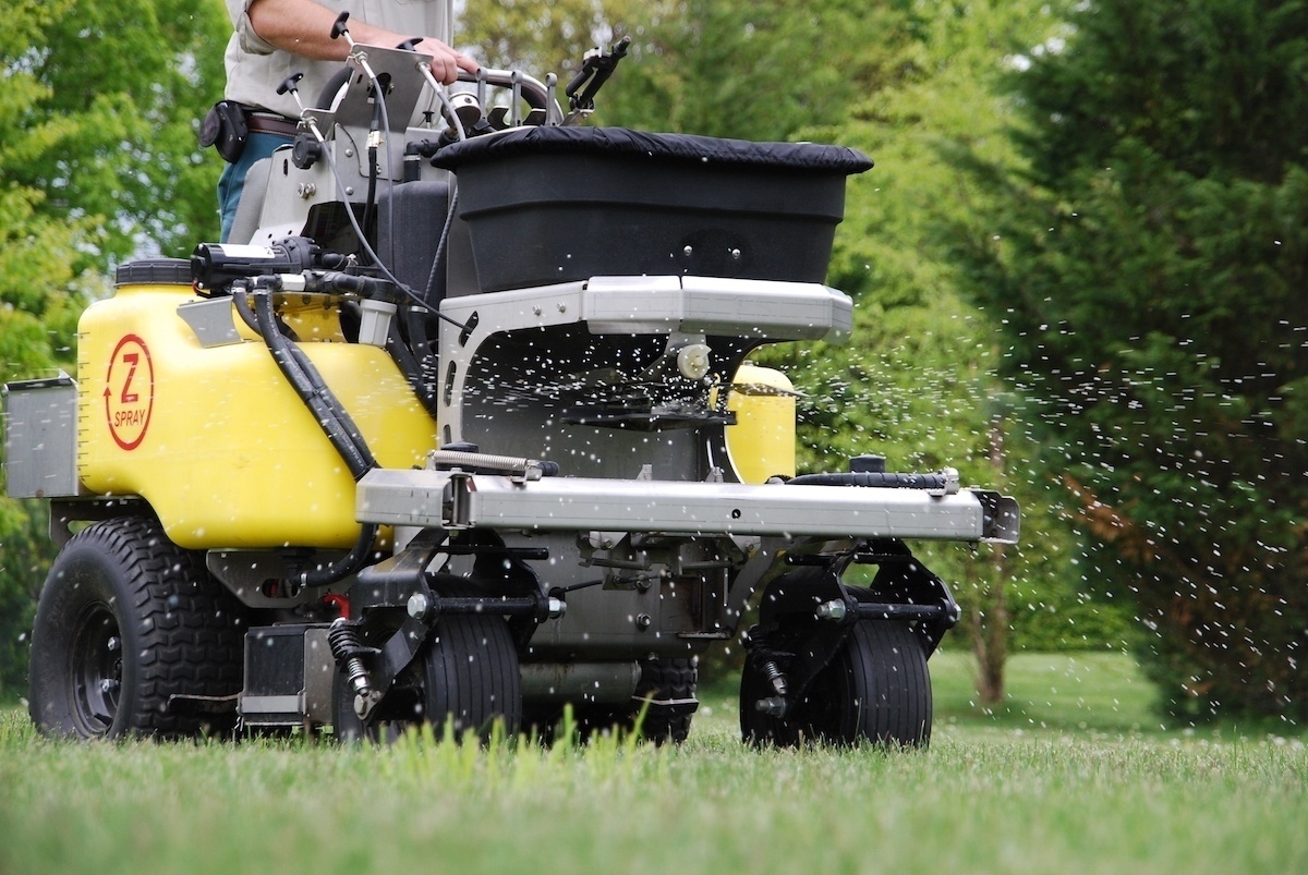 lawn care technician spreads granular fertilizer