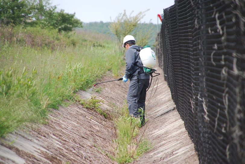 vegetation management technician spraying weed control along fence line