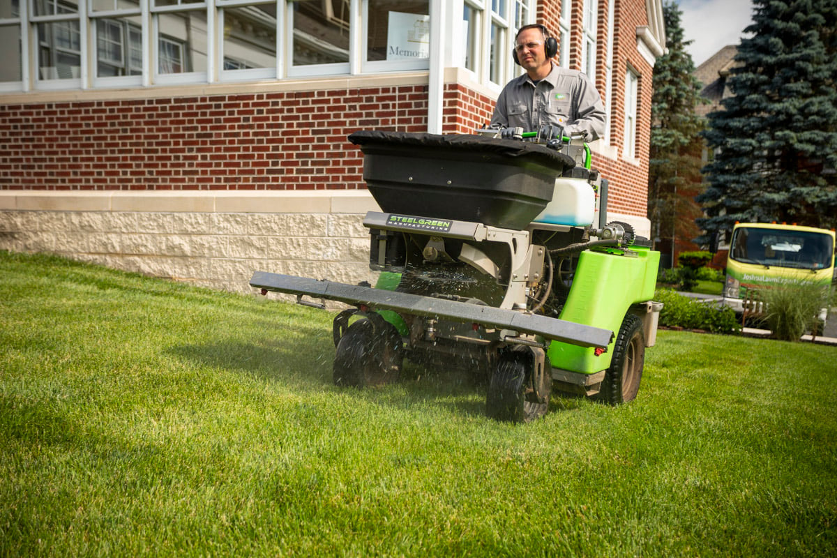 lawn care technician puts down grub control with ride on spreader 