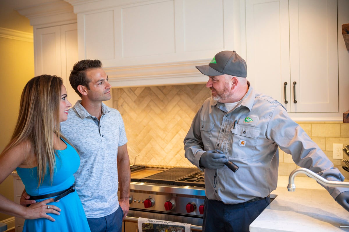 pest control technician talks with homeowners in kitchen