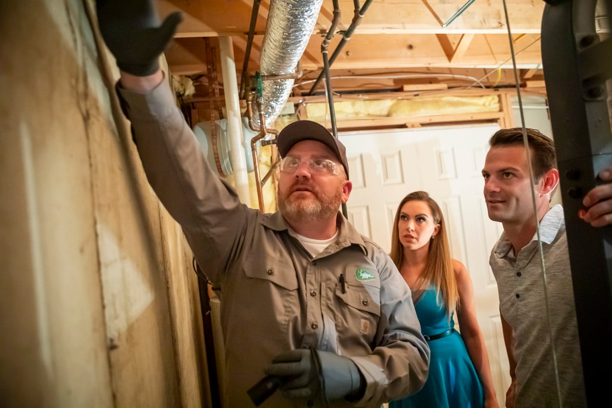 pest technician inspects home with clients