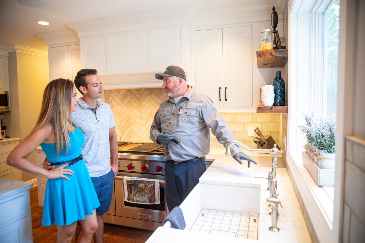 pest control technician inspects kitchen with customers