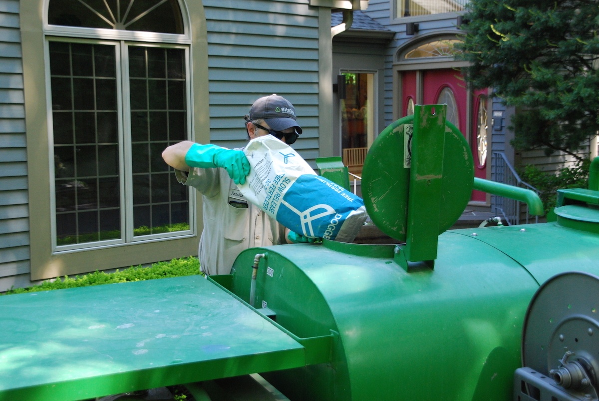 plant health care expert pours fertilizer into spreader for tree